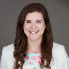 A woman in a white suit jacket smiles.